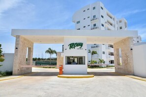 A hotel entrance with a prominent sign, a reception desk, and a modern building in the background. - Tropical Apartment with Pool | Hemingay Beach | TEPUY Juan Dolio (Playa Juan Dolio)