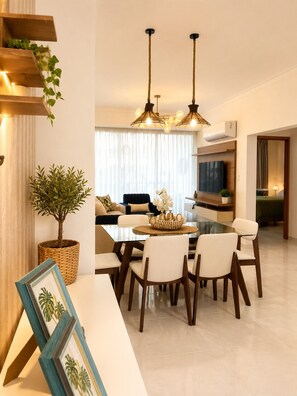 A modern living room with a dining area, featuring a large TV, a fireplace, and a dining table with chairs. - Tropical Apartment with Pool | Hemingay Beach | TEPUY Juan Dolio (Playa Juan Dolio)