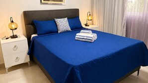 A hotel room with a bed, a nightstand, a lamp, a painting, and a window with curtains. - Tropical Apartment with Pool | Hemingay Beach | TEPUY Juan Dolio (Playa Juan Dolio)