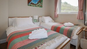 A hotel room with two beds, a painting on the wall, a window with curtains, and a bedside table with a lamp. - Kippy Cottage (Truro)