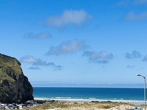 A coastal view with a rocky cliff, beach, and ocean. - Kippy Cottage (Truro)