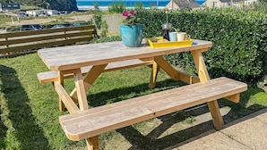 A wooden picnic table with benches, a blue vase, and a yellow tray with food items. - Kippy Cottage (Truro)
