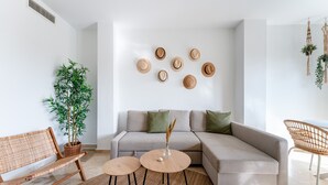 Een moderne woonkamer met een bank, twee ronde tafels, een rieten bankje en een potplant.