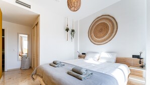 Een moderne slaapkamer met een groot bed, een geweven wanddecoratie en een kleine plant.