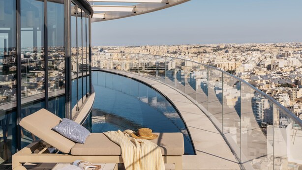 Una piscina infinita moderna con barandilla de vidrio y vistas a un paisaje urbano.