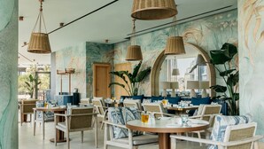 Un restaurante con mobiliario de mimbre, mesas redondas y un mural en la pared.