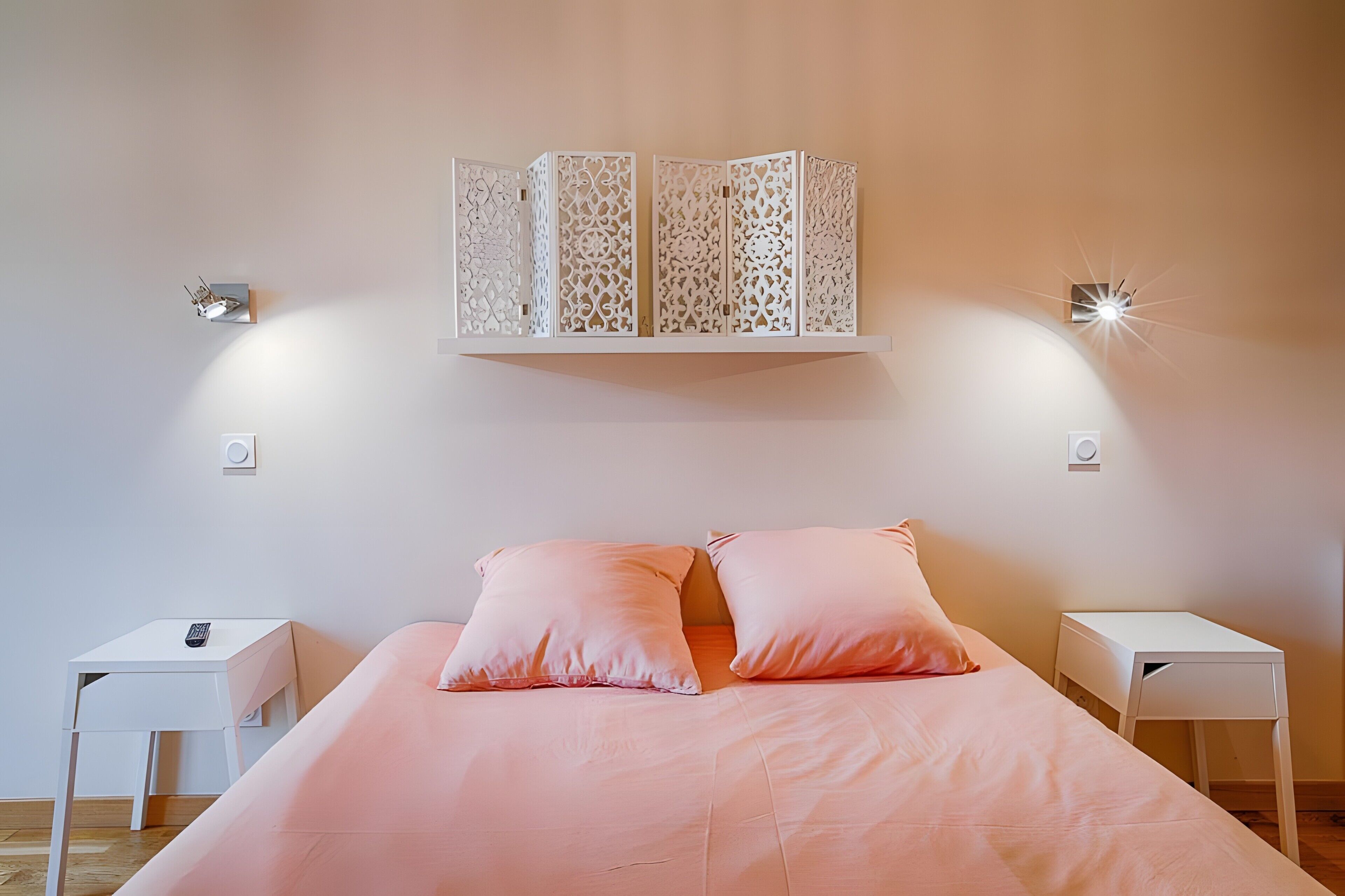 Une chambre à coucher comprenant un lit, deux tables de chevet, un paravent décoratif et des lampes fixées au mur.