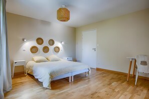 Un dormitorio con cama, mesitas de noche, una silla, una puerta y una lámpara fijada a la pared.