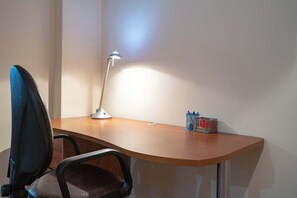 Ein Büro mit Ecklage, ausgestattet mit Schreibtisch, zwei Stühlen, einer Schreibtischlampe und einer kleinen Aufbewahrungsbox.