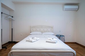 A neatly made bed with white linens and towels, a metal headboard, a small bedside table, and an air conditioning unit on the wall. - Blue Harmony 3BR • Heart of Athens by ΜΡS (Athina)