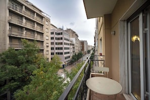 A balcony with a table and chairs, overlooking a street with buildings and trees. - Blue Harmony 3BR • Heart of Athens by ΜΡS (Athina)