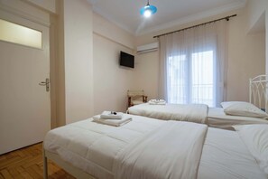 Ein Hotelzimmer mit zwei Betten, einem Fernseher, einer Klimaanlage und einem Vorhangfenster.