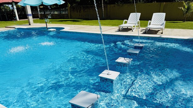 A swimming pool with clear blue water, a water fountain, and two white lounge chairs. - Beachfront House in El Tamarindo (El Tamarindo)