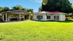 A two-story house with a red roof, a covered patio with outdoor furniture, and a well-maintained lawn. - Beachfront House in El Tamarindo (El Tamarindo)