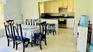 A dining area with a table set for four, surrounded by chairs. A kitchen with cabinets and appliances is visible in the background. - Beachfront House in El Tamarindo (El Tamarindo)