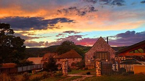 Un edificio rústico de piedra con techo a dos aguas, una estructura de madera con techo inclinado y un portón que dice 'GITES'.