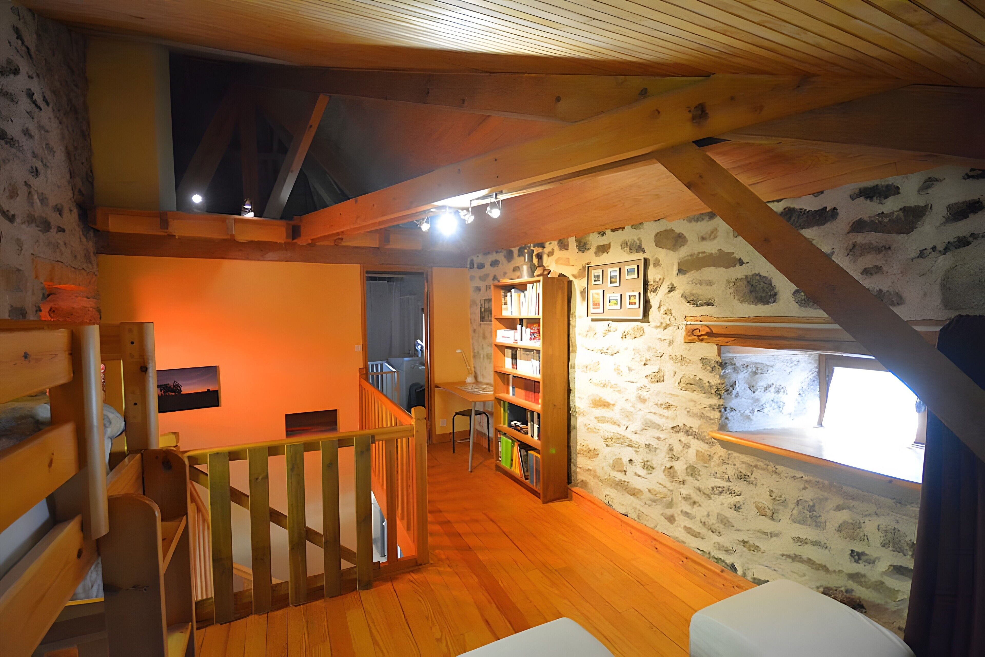 Una habitación con techo de madera, paredes de piedra, una estantería y un ventanal.