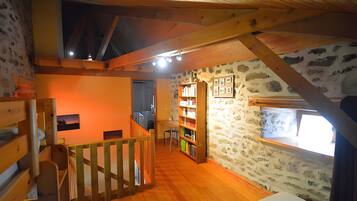 Una habitación con techo de madera, paredes de piedra, una estantería y un ventanal.