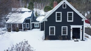 Uma casa de dois andares com fachada escura, detalhes em branco e uma chaminé.