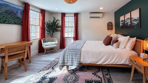 Quarto com cama grande, escrivaninha, cadeira, tapete e ar condicionado fixado na parede.