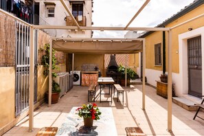 A covered outdoor patio with a table and benches, surrounded by potted plants and a washing machine. - Casa Bruno Terrace Charm by Wonderful Italy (Catania)
