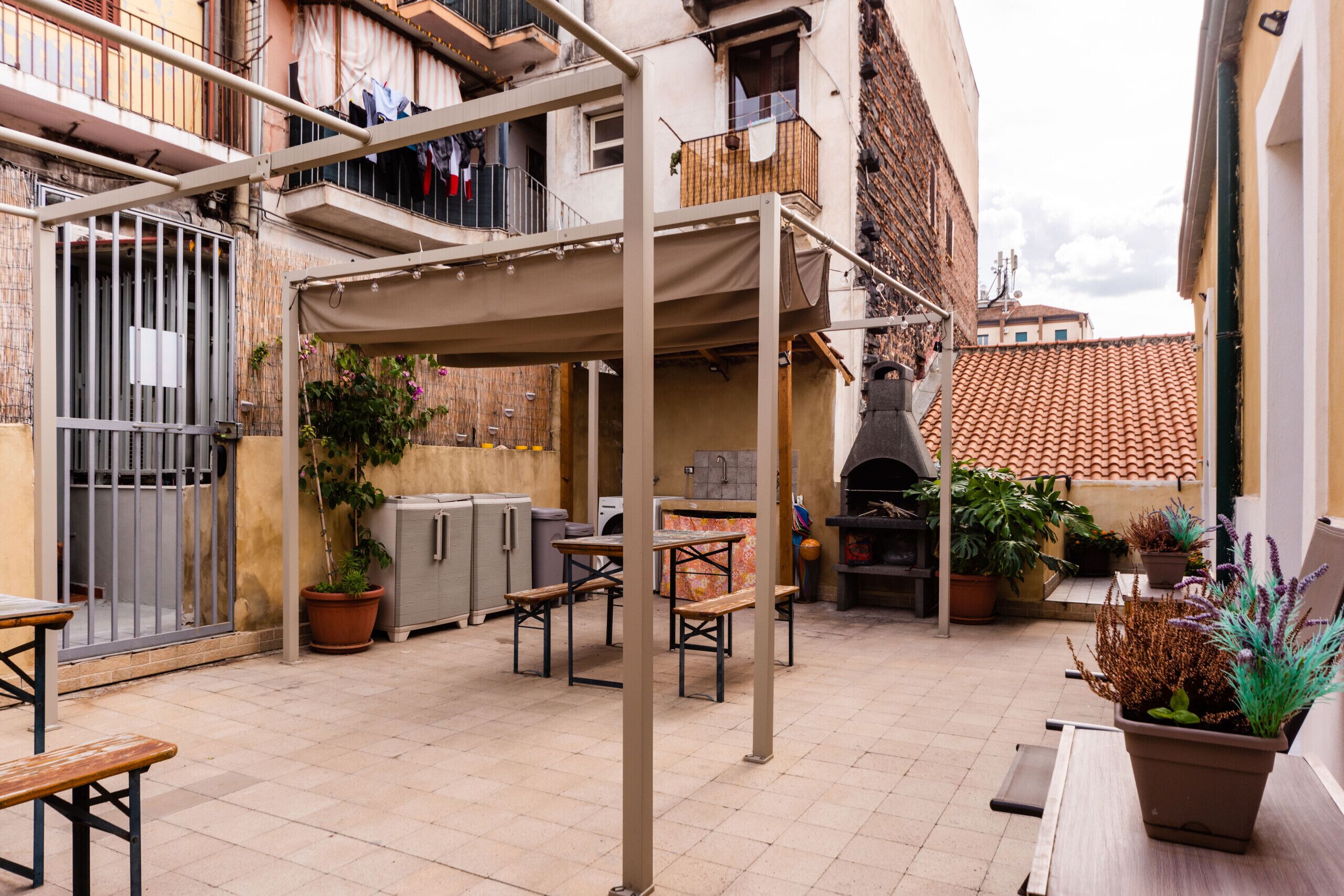 Un espace extérieur aménagé en terrasse, avec une pergola, des sièges, des plantes en pot et un four en briques.