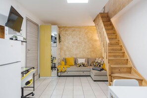 A compact living space with a sofa, a TV, a wooden staircase, and a kitchen area. - Casa Bruno Terrace Charm by Wonderful Italy (Catania)