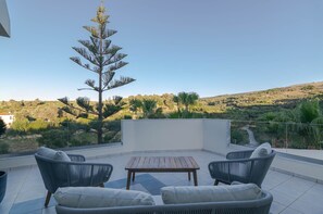 Eine Terrasse im Freien mit Korbmöbeln, einem Holztisch und Blick auf eine hügelige Landschaft.