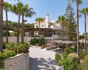 A modern villa with a stone wall, a pergola, and lush greenery. - Kipo Paradiso 6 Spa Yoga & Gym Resort (Rethymno)