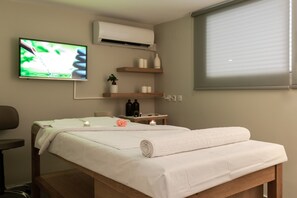 Ein ordentlich eingerichtetes Zimmer mit einem Bett, einem Fernseher, einer Klimaanlage und einem Fenster mit Jalousien.