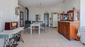 A dining area with a table, chairs, a chandelier, a vintage radio, and a wooden cabinet. - Gallery House (Viannos)