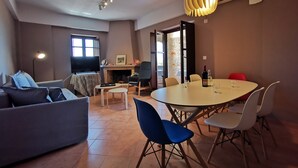 A living room with a sofa, a TV, a fireplace, and a dining area with chairs and a table. - Anaroussa Diros Villa (East Mani)