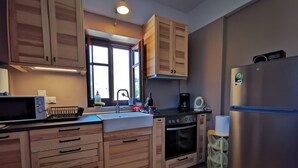 A kitchen with wooden cabinets, a stainless steel refrigerator, a microwave, a sink, and a window. - Anaroussa Diros Villa (East Mani)