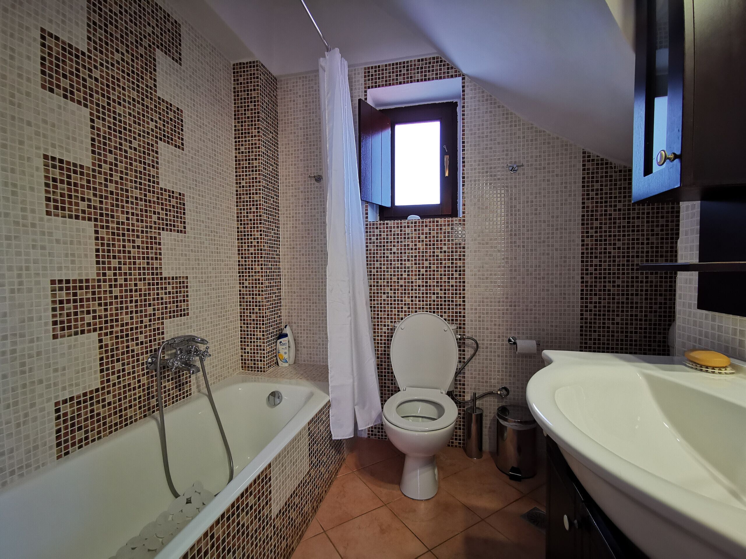 A bathroom with a bathtub, toilet, and sink, tiled walls, and a window.