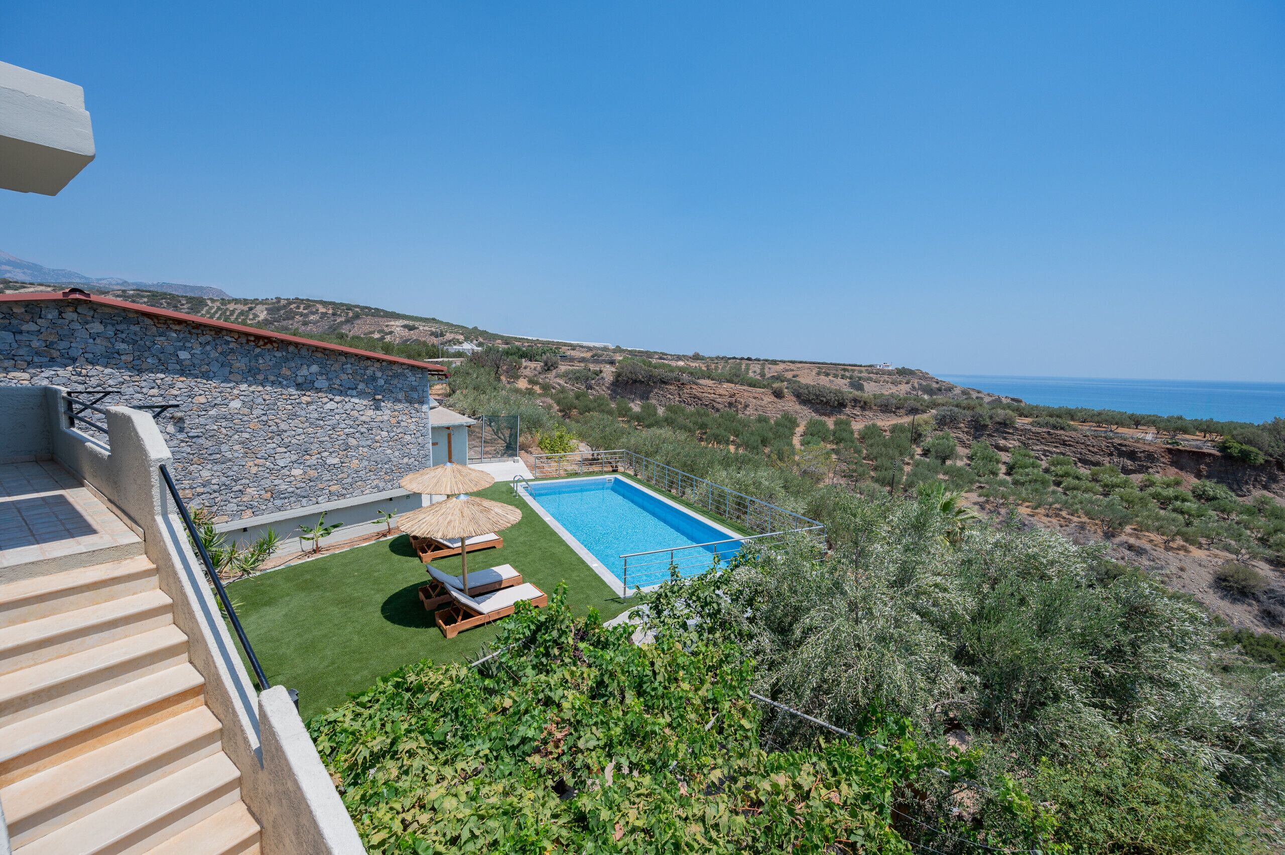 Une piscine bordée d’un muret en pierre, une pelouse et une vue sur la mer.