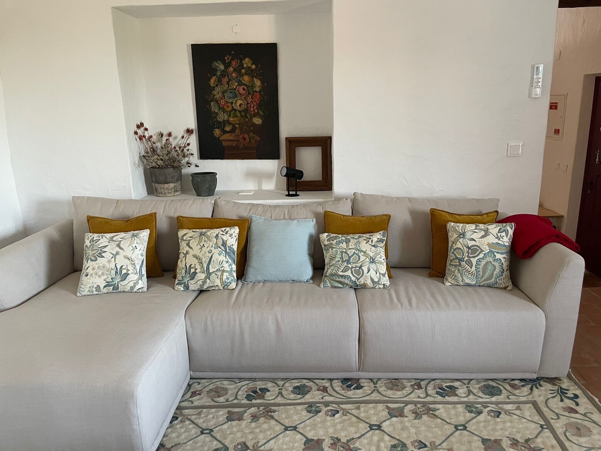 Uma sala de estar com sofá, almofadas estampadas, um quadro floral e uma pequena mesa.