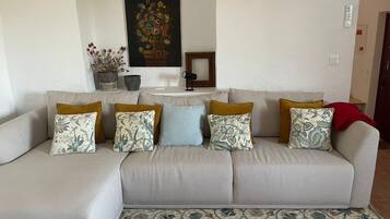 Uma sala de estar com sofá, almofadas estampadas, um quadro floral e uma pequena mesa.