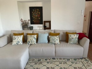 A living room with a sofa, patterned cushions, a floral painting, and a small table. - Monte Barriga: Cozy Retreat with Private Pool and Air Conditioning (Beja)
