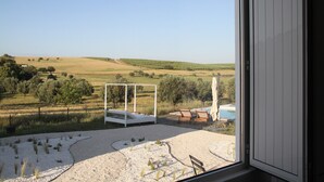 Een kamer met uitzicht op een landelijk landschap, een wit bed en een zwembad.