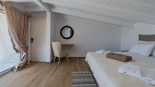 A bedroom with a bed, a chair, a mirror, and a window with curtains. - Mythos 4 (Agios Vasileios)