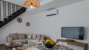 A modern living room with a staircase, a dining area with a table set for two, a sofa, and a flat-screen TV mounted on the wall. - Mythos 4 (Agios Vasileios)