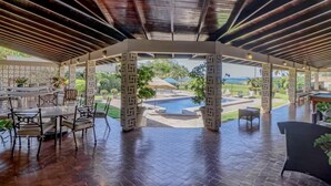 Une terrasse extérieure couverte, dotée d’une piscine, de coins salon et offrant une vue sur le paysage environnant.