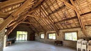 Um quarto amplo no sótão, com vigas de madeira aparentes, paredes de pedra e grandes janelas.