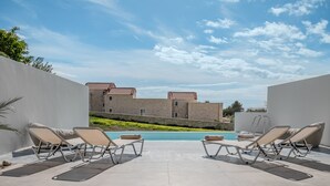 Ein Poolbereich mit Liegestühlen und Blick auf ein Gebäude mit roten Ziegeldächern.