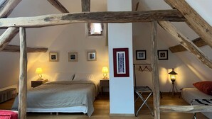 Un dormitorio con techo inclinado, vigas de madera, una cama, dos mesitas de noche con lámparas y cuadros enmarcados en las paredes.