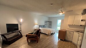 A room with a TV, a bed, a chair, a lamp, a ceiling fan, and a kitchen area. - Cozy studio in Port St. Lucie with AC -WiFi for relaxing stays (Port St. Lucie)