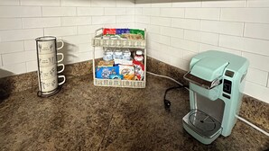 Una cocina con armarios blancos, una cafetera, un escurreplatos para tazas y una cesta de aperitivos.