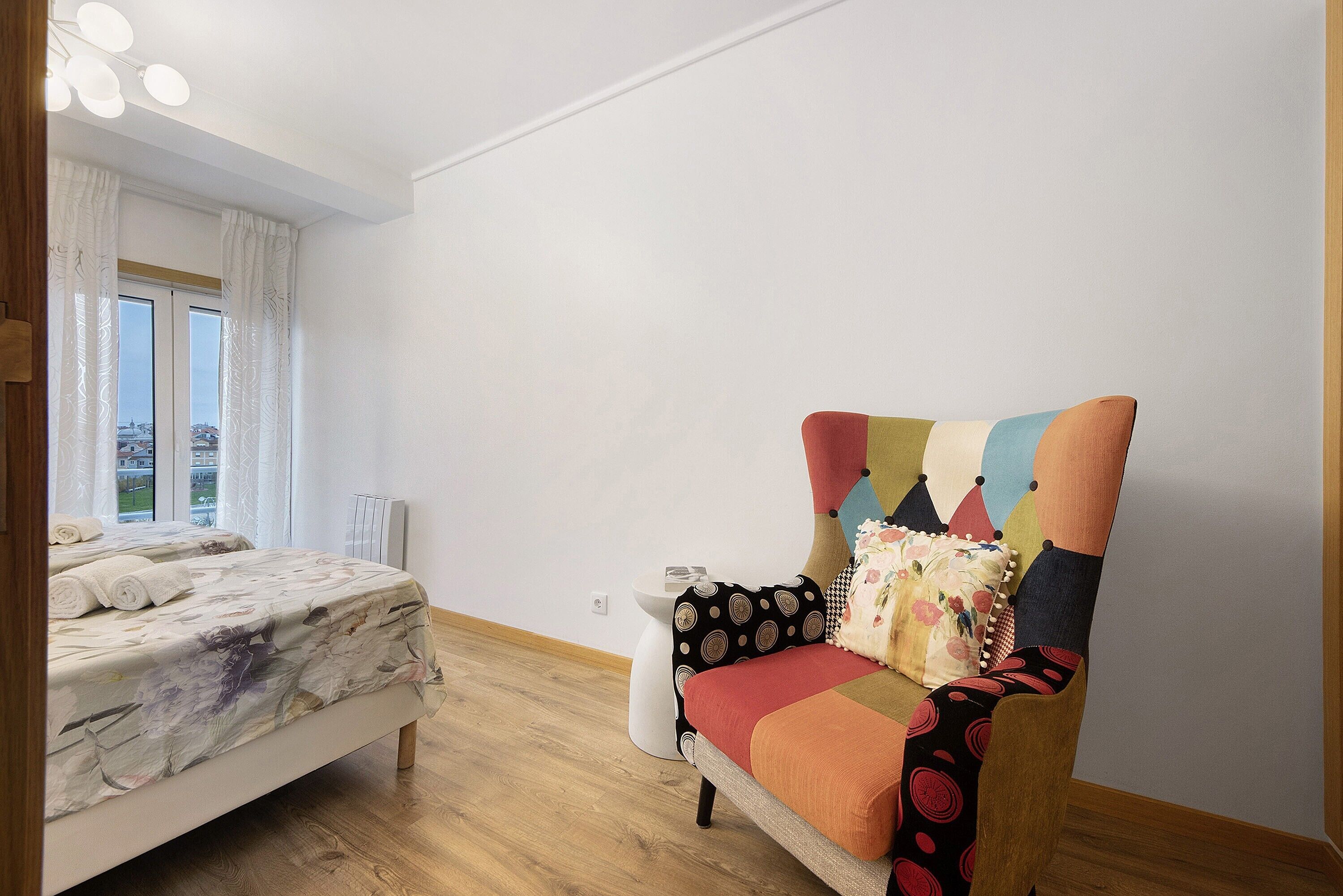 A bedroom with a bed, a chair, a radiator, and a window.