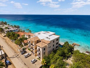 Un hôtel à plusieurs étages, doté d’un toit plat, situé près d’une plage aux eaux bleues et cristallines.