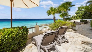 A seaside patio with two lounge chairs and a large umbrella, overlooking a clear blue ocean. - Bellevue Penthouse 10 (Kralendijk)